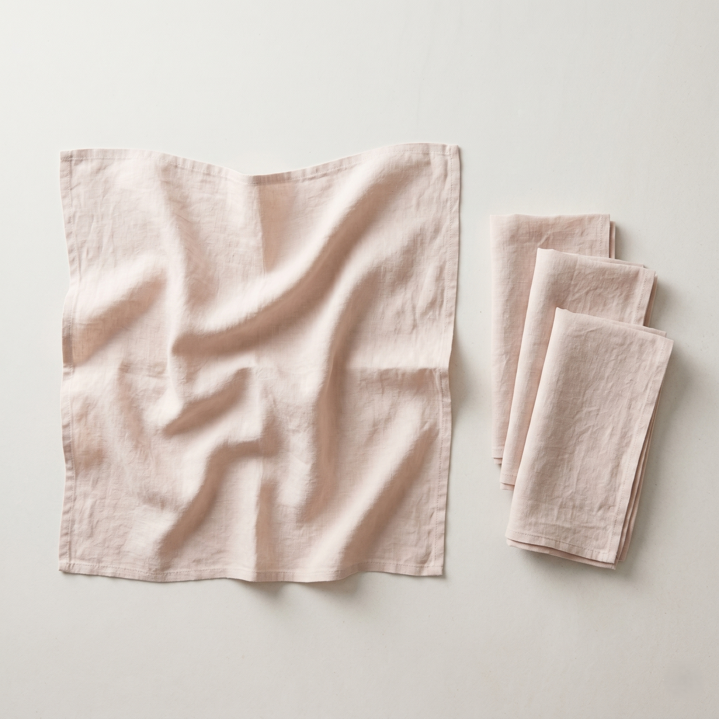 Stack of four folded blush plain linen napkins in soft warm-pink pure linen