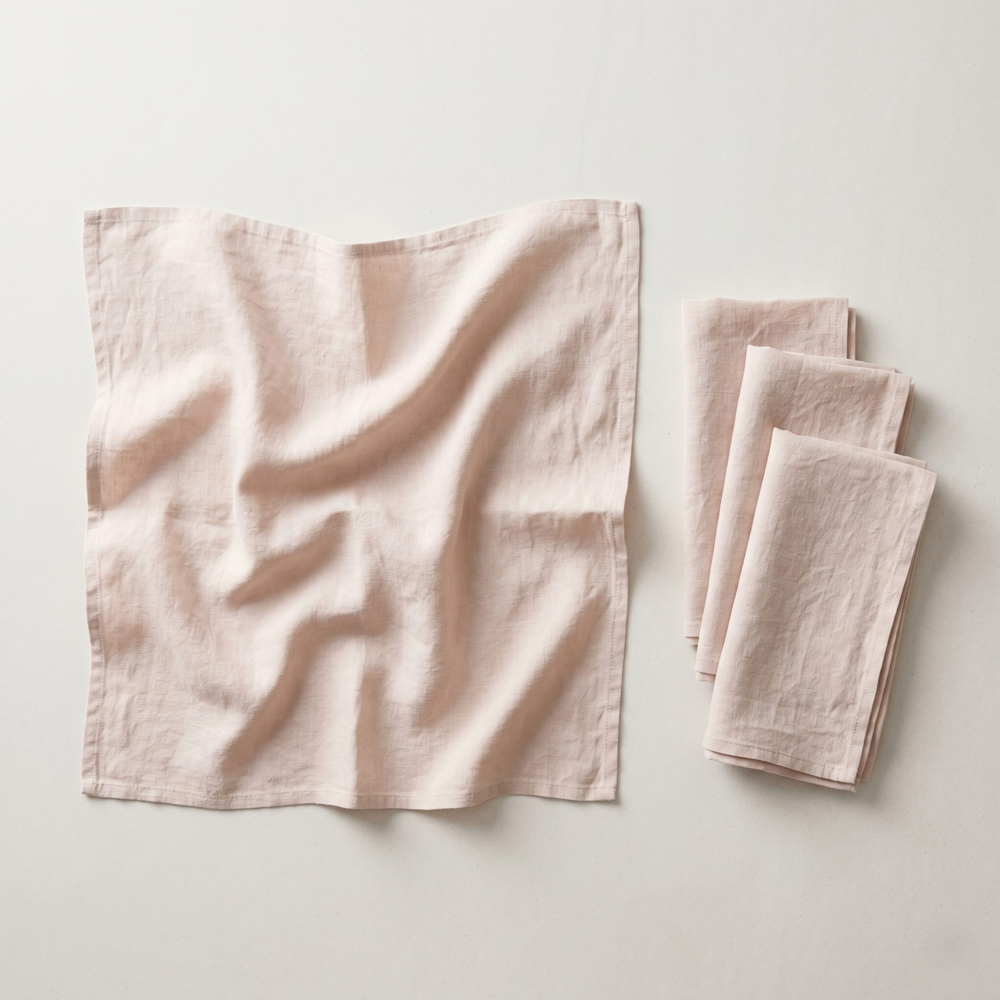 Stack of four folded blush plain linen napkins in soft warm-pink pure linen