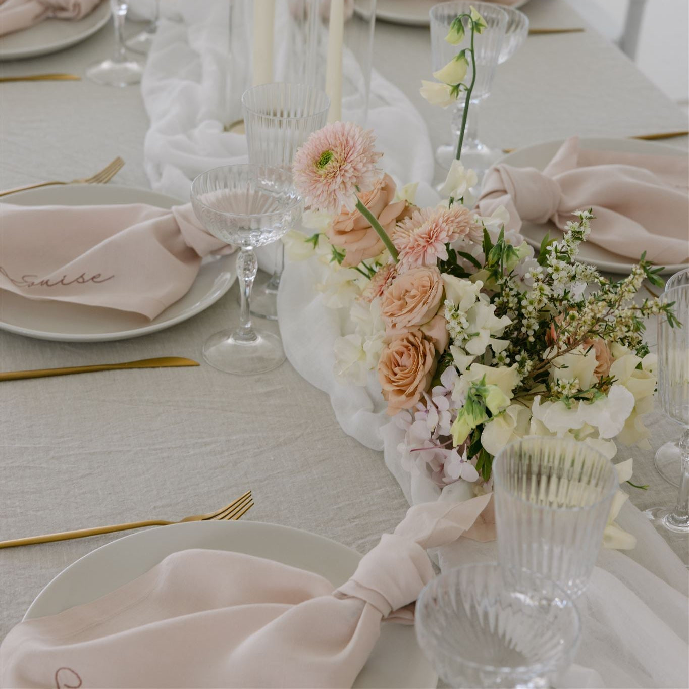 Wedding table with blush linen napkins, gold cutlery, ribbed glassware and a soft pastel floral centrepiece